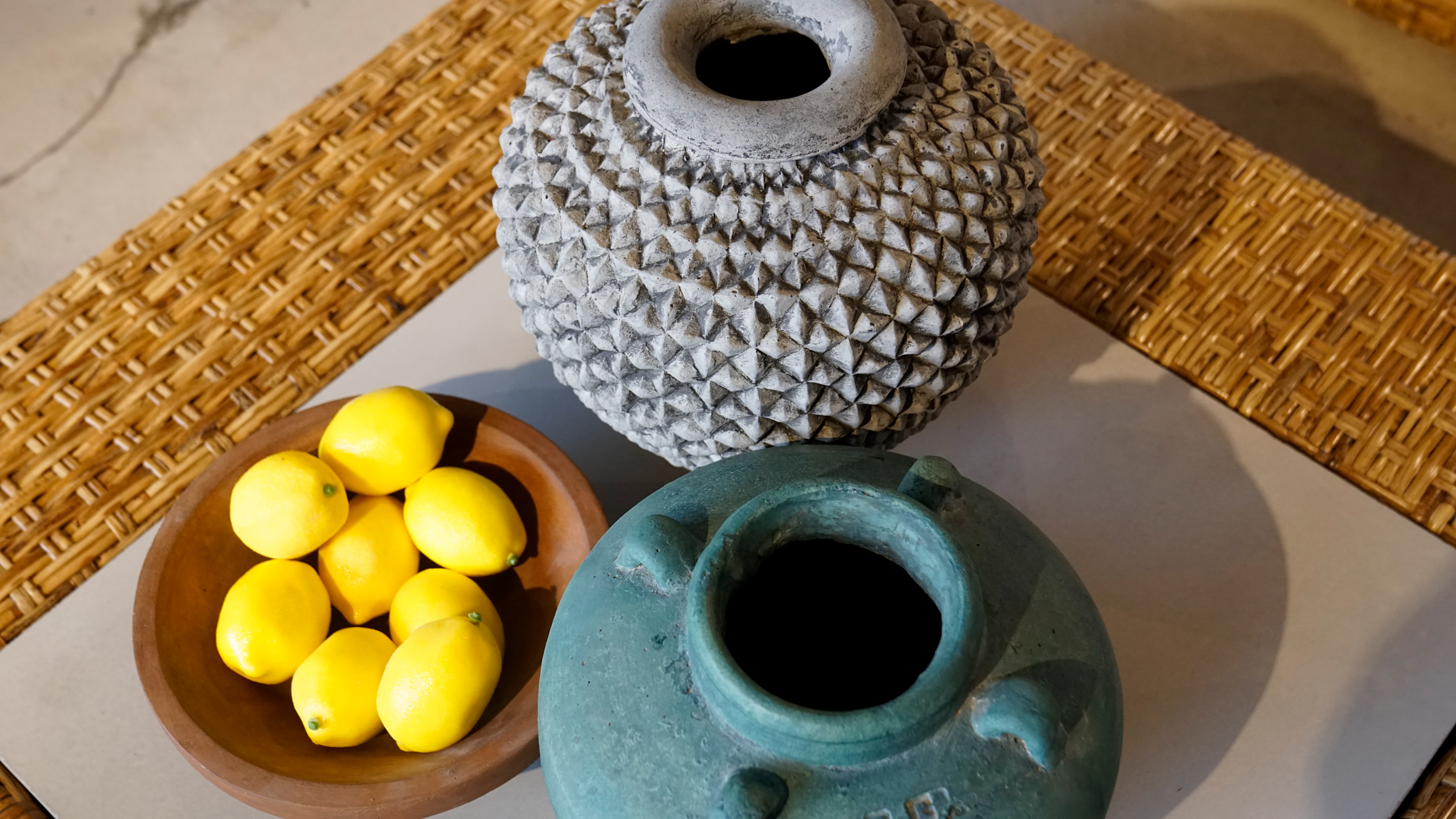 Overhead shot of textured clay vases and a wooden bowl filled with lemons.