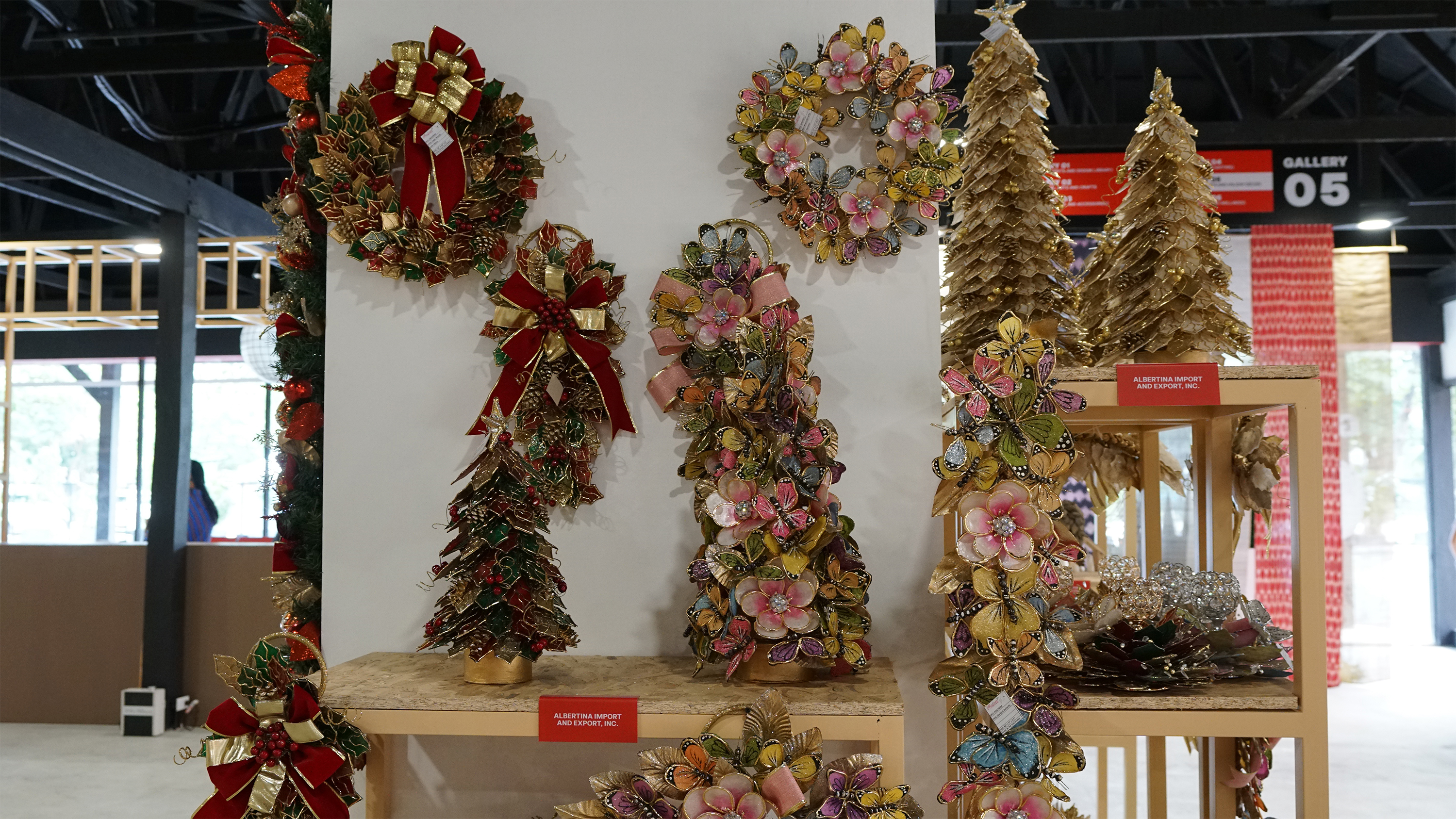 Holiday display featuring gold and red wreaths and cone trees adorned with butterflies and flowers.